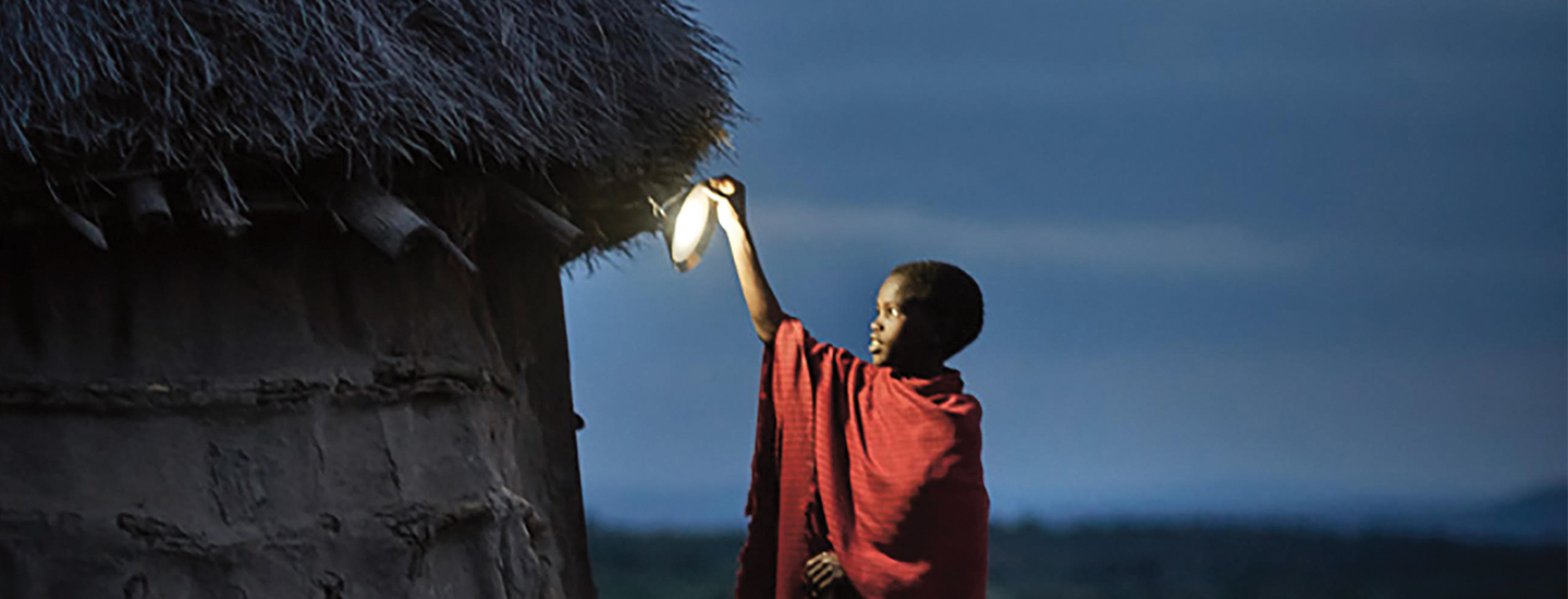 young African child adjusting a solar lamp on a home during dusk