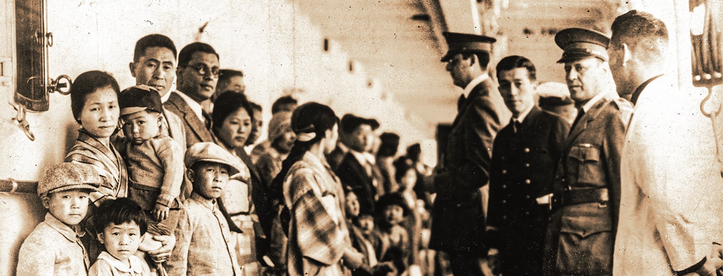 Black and white photo of Chinese immigrant families lined up against a wall