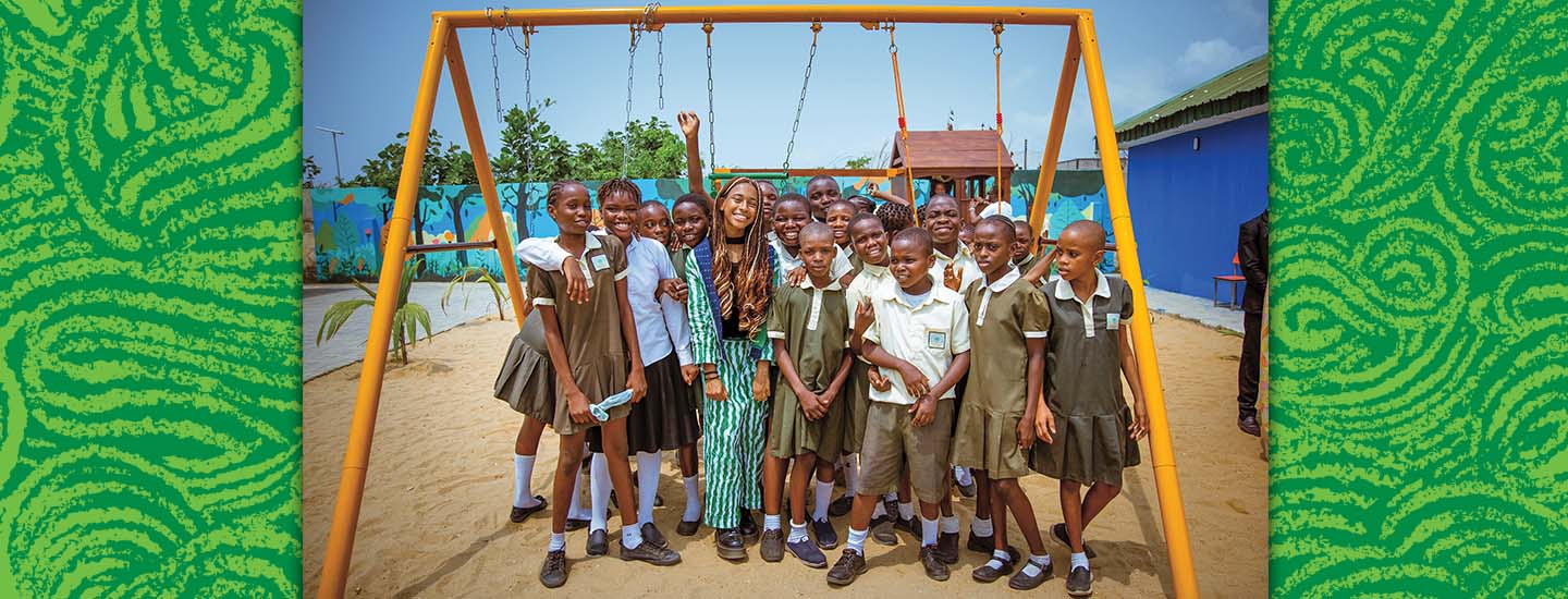 A woman and students in school uniforms pose together on a playground with a swing set