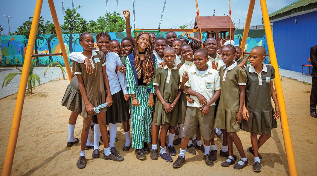 A teacher poses with students in school uniforms on a playground with colorful murals