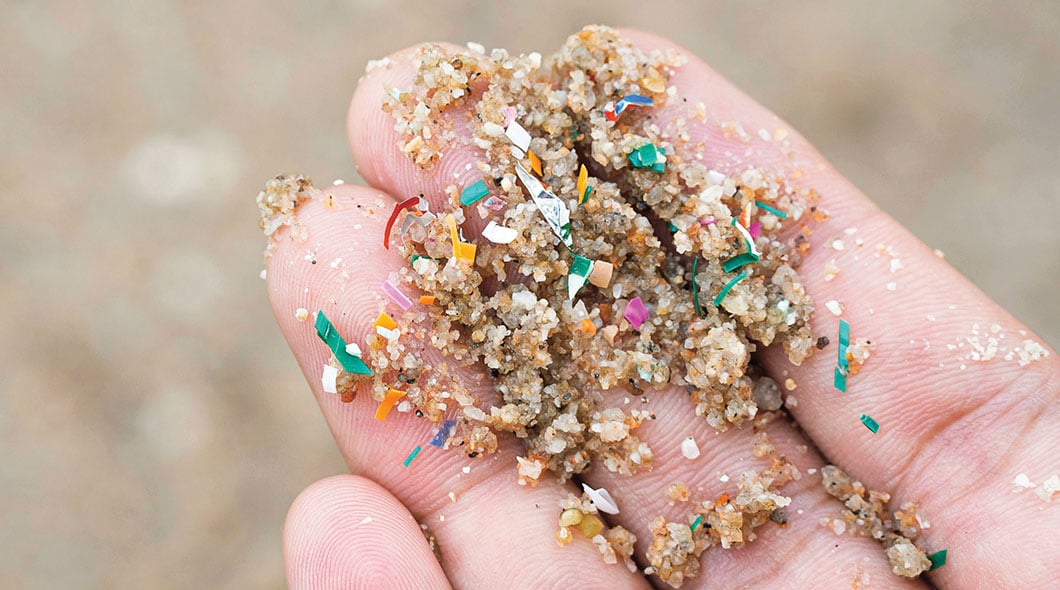 A hand holds sand mixed with colorful microplastic pieces