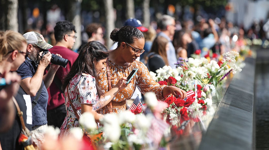 People place flowers and small American flags along the 9/11 Memorial reflecting pool edge