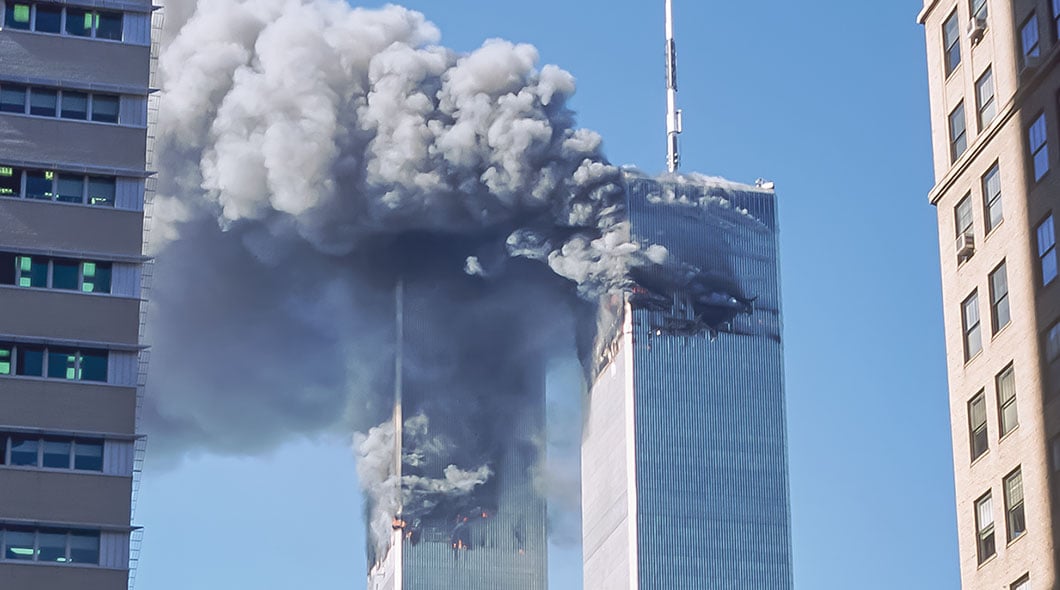 Historical photo of the Twin Towers with flames and large plumes of smoke rising from both buildings