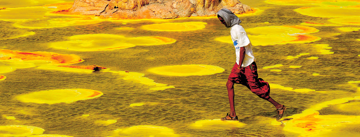 Photo of a person walking on mineral deposits to avoid yellowish-green toxic water